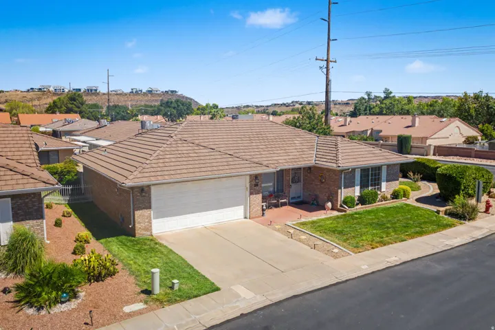 Brick exterior with a tiled roof, attached garage, concrete driveway, and a landscaped front yard