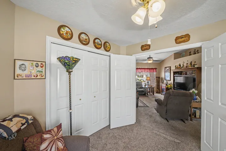 Carpeted flooring, bi-fold closet doors, ceiling fan with light fixture, and arched doorway