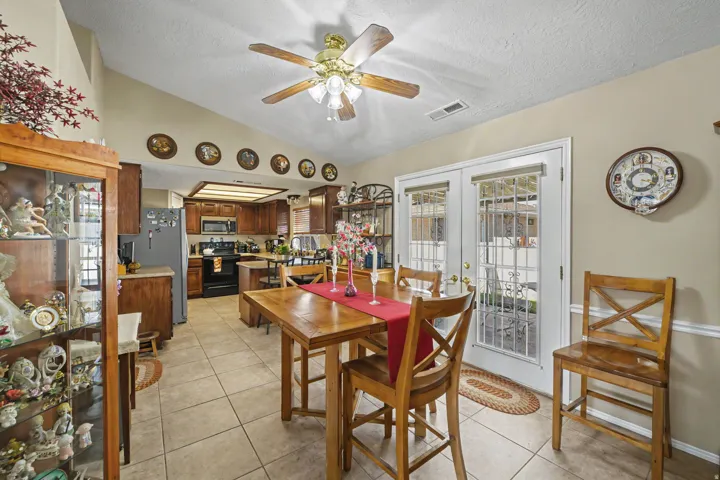 Vaulted ceiling, ceiling fan, wood-finish cabinetry, tile flooring, and double French doors with security bars