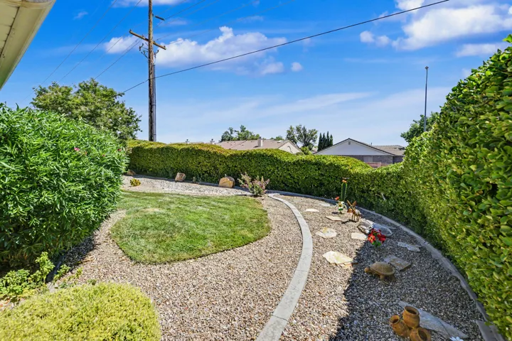 Landscaped yard with gravel pathways, defined by concrete edging, manicured hedges, and a central grass area