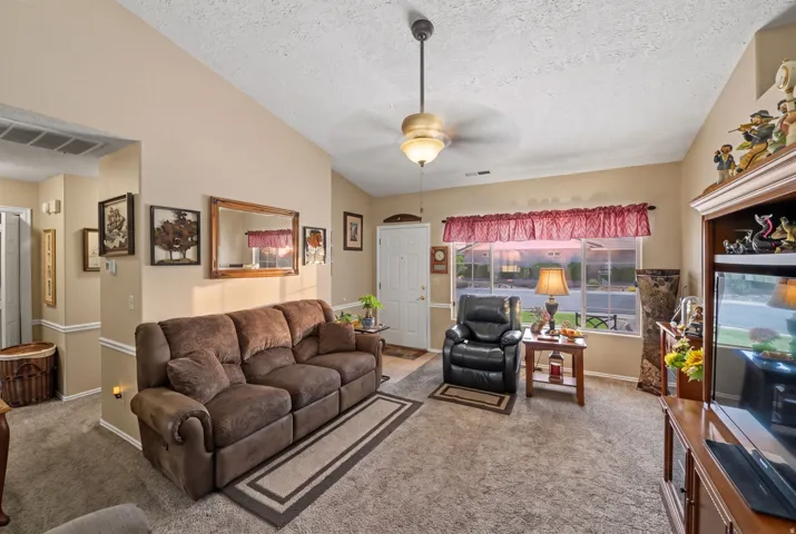 Vaulted ceiling with an attached ceiling fan, large front-facing window, and wall-to-wall carpeting