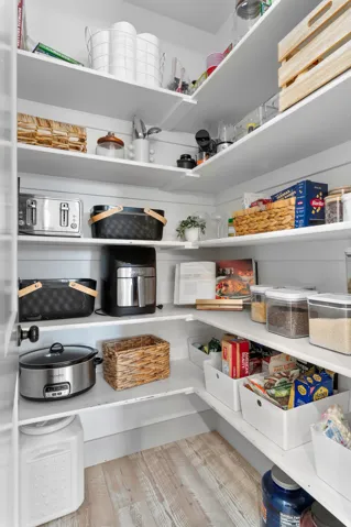 Corner pantry featuring white shelving, wood-finish flooring, and shiplap wall accents