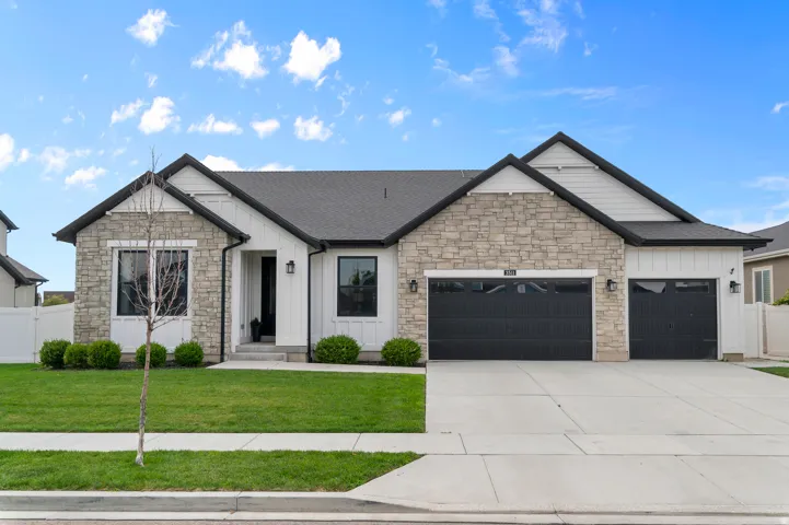 Contemporary exterior featuring stone and vertical panel siding, dark-frame windows, a two-car garage, and a separate single-car garage
