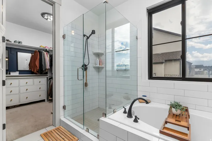 Walk-in shower with clear glass enclosure and subway tile surround, deep soaking tub with matte black fixtures, and a large window with black framing