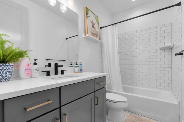 Bathroom featuring a white subway tile tub surround, white bathtub, vanity with a white countertop, and dark-finish cabinetry with gold-tone hardware