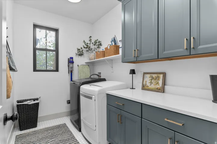 Dedicated laundry room featuring soft-close cabinetry in slate blue with brass hardware, white quartz countertops, a front-load washer, and ample storage