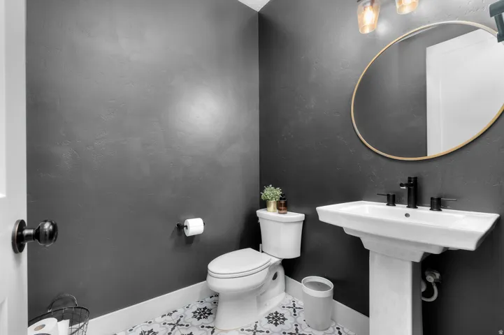 Pedestal sink with matte black fixtures, round framed mirror, and patterned floor tile