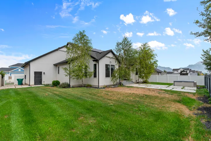 Expansive rear yard featuring a large grass area, concrete patio, and a white privacy fence