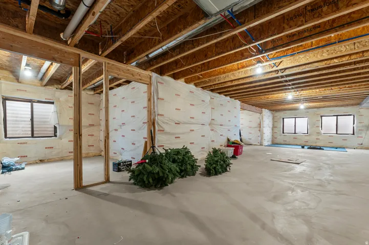 Unfinished basement featuring exposed wood joists, concrete flooring, framed interior walls, multiple windows, and exposed ductwork