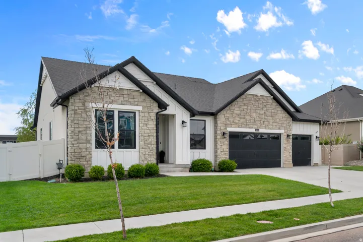 Stone and board-and-batten exterior with dark-framed windows, a dark shingle roof, and a concrete driveway