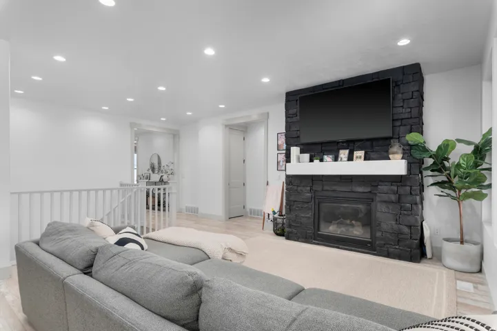 Living area featuring a floor-to-ceiling black stone fireplace with a white floating mantel, recessed lighting, light wood-finish flooring, and a white railing