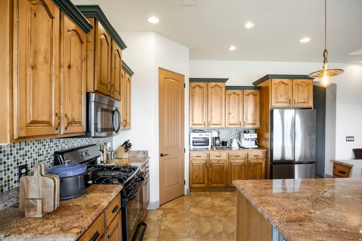 Kitchen featuring wood cabinetry with crown molding, stainless steel appliances, mosaic tile backsplash, and stone countertops