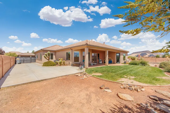 Rear exterior featuring a covered patio, expansive lawn, and arid landscaping
