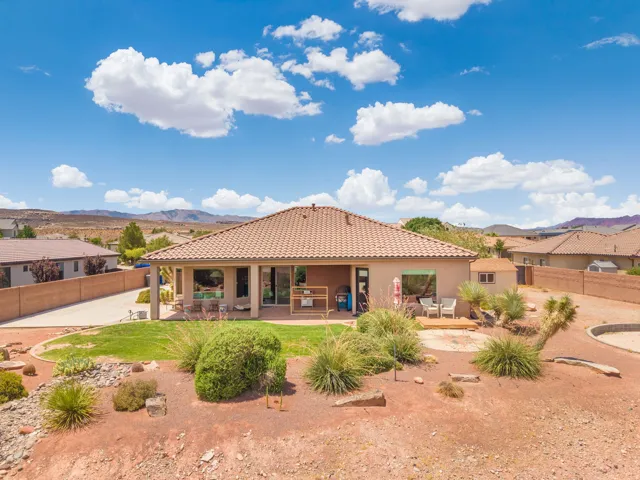 Rear exterior featuring a covered patio, xeriscaped landscape, mature desert plantings, and a detached storage shed