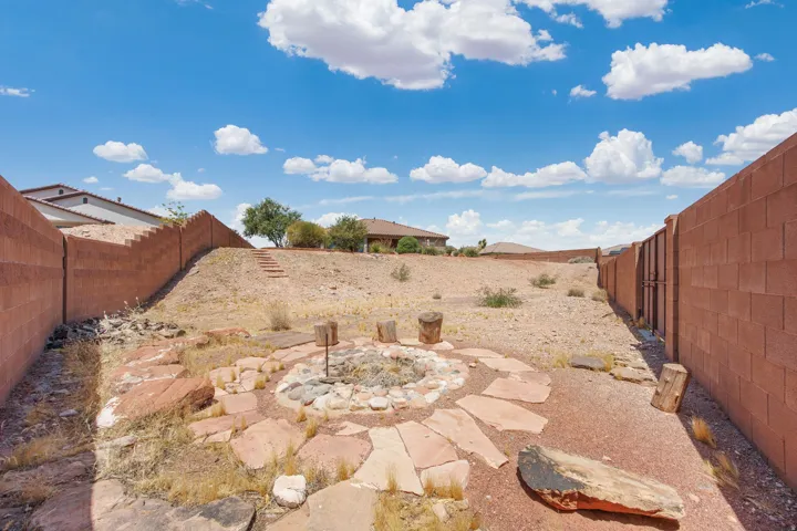 Expansive backyard featuring a stone-lined fire pit, natural rock landscaping, and a sloped terrain