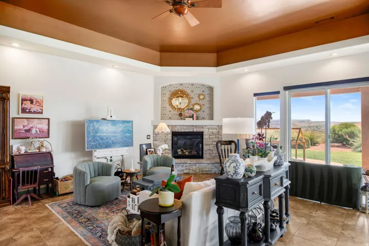Living area featuring a stone-clad fireplace with an arched mosaic tile surround, large sliding glass doors, a tray ceiling with recessed lighting, and tile flooring