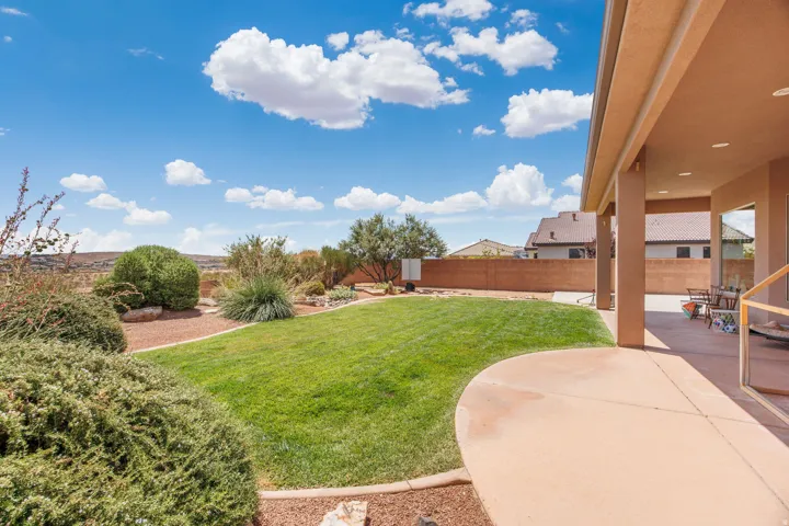 Expansive backyard featuring a manicured lawn, established desert landscaping, and a substantial covered patio with recessed lighting