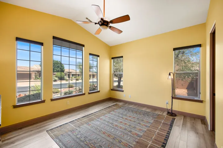 Vaulted ceiling with a ceiling fan, light-toned wood-finish flooring, and multiple windows with dark trim and grilles