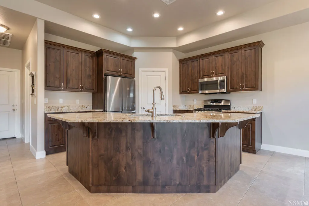 Spacious kitchen featuring an angular island with an undermount sink, granite countertops, stainless steel appliances, and abundant wood cabinetry