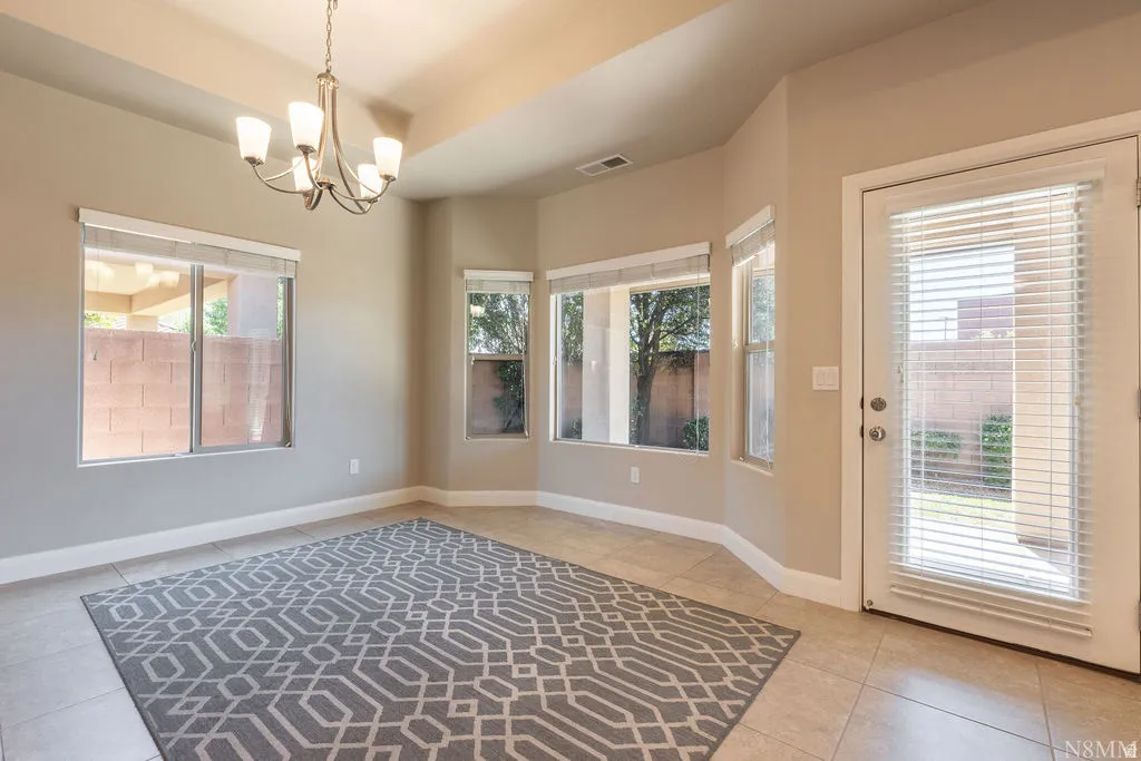 Recessed ceiling with an overhead chandelier, multiple windows with blinds, a glass-paned door, and tiled flooring