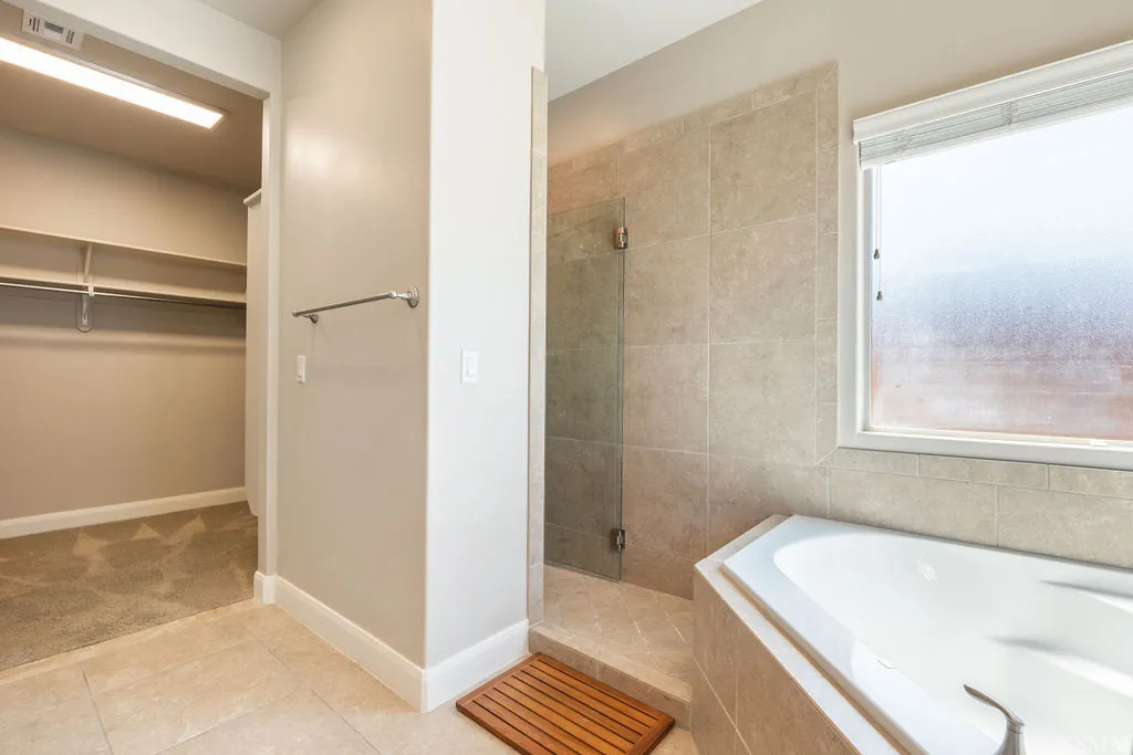 Luxurious master bath featuring a spa-inspired walk-in shower with frameless glass enclosure, a soaking tub with surround, and tile finishes throughout
