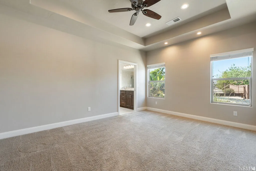 Recessed lighting, ceiling fan, two windows, and an en-suite bathroom featuring a wood-finish vanity