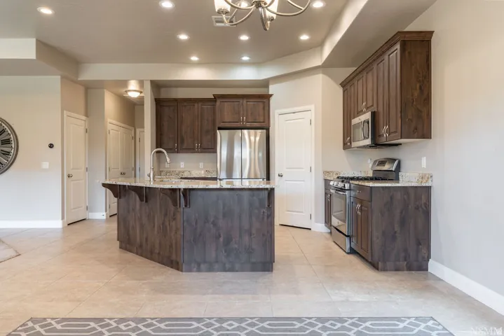 Kitchen featuring dark wood-finish cabinetry, stainless steel appliances, granite countertops, a kitchen island with a sink, and recessed lighting