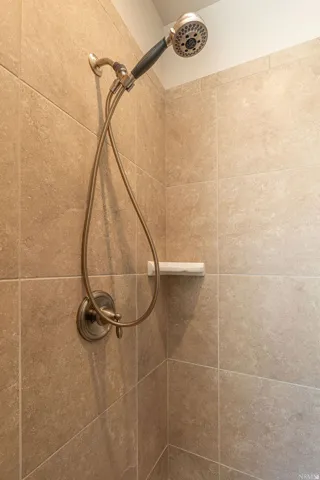 Tiled shower enclosure featuring a handheld showerhead, wall-mounted shower faucet, and a built-in corner shelf