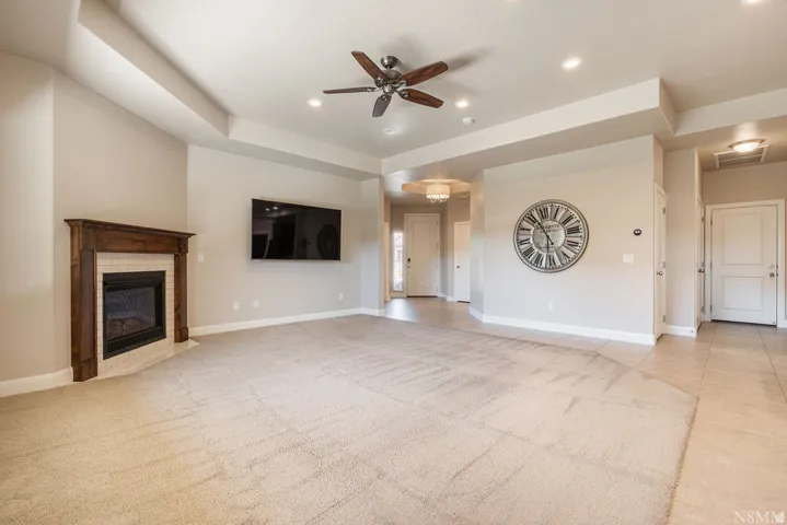 Tray ceiling, recessed lighting, ceiling fan, wood-mantled fireplace with tile surround, and tile flooring