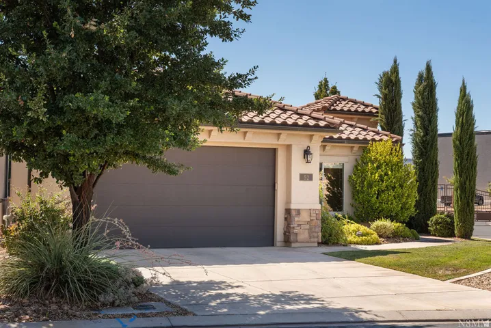Stucco exterior with a tile roof, an attached garage, a concrete driveway, and established front landscaping