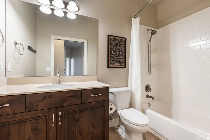 Bathroom featuring a single vanity with wood-finish cabinetry, a large mirror, a combined shower and tub, and subway tile surround