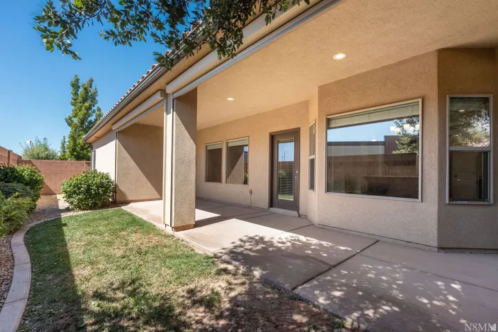 Expansive covered patio with stucco exterior and recessed ceiling lighting, overlooking manicured lawn with mature landscaping and curved hardscape edging