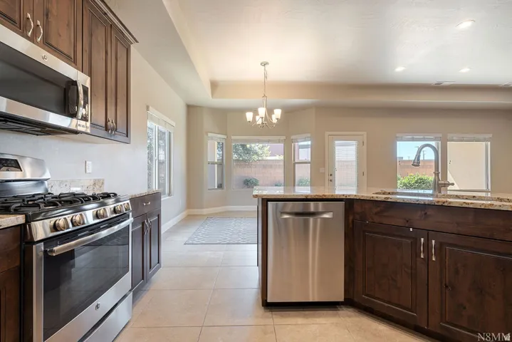 Spacious kitchen featuring custom wood cabinetry, stainless steel appliances including a gas range and built-in dishwasher, granite countertops, and a large center island with prep space