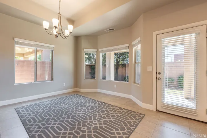 Recessed ceiling with an overhead chandelier, multiple windows with blinds, a glass-paned door, and tiled flooring