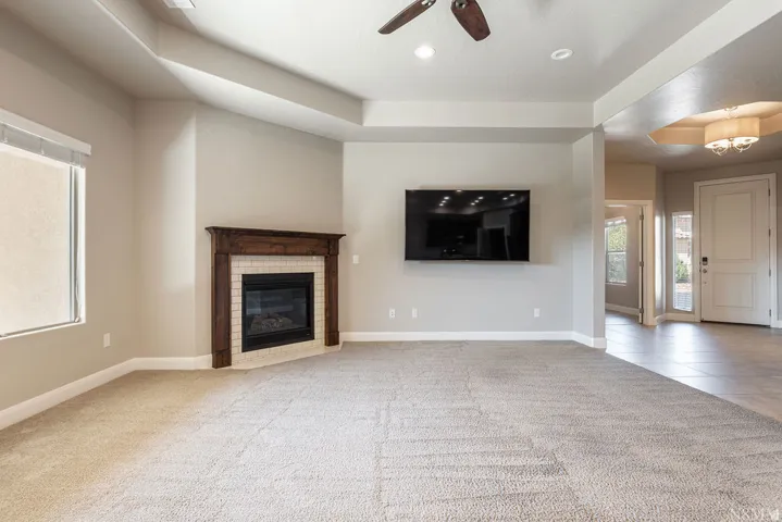 Recessed lighting, ceiling fan, fireplace with wood-finish mantel and tile surround, and tray ceiling detail