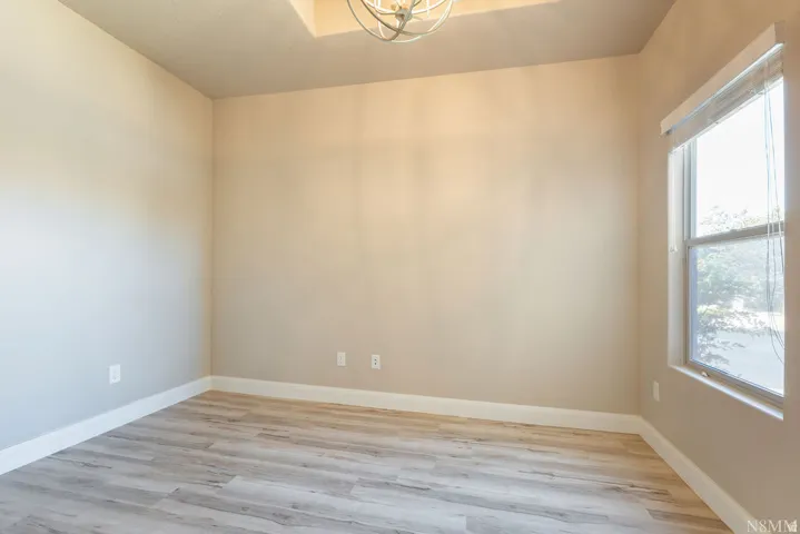 Recessed ceiling with an ornate light fixture, wood-finish flooring, and a large window