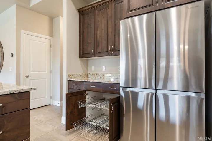 Stainless steel refrigerator, upper and lower wood-finish cabinetry, granite countertops, and tile flooring