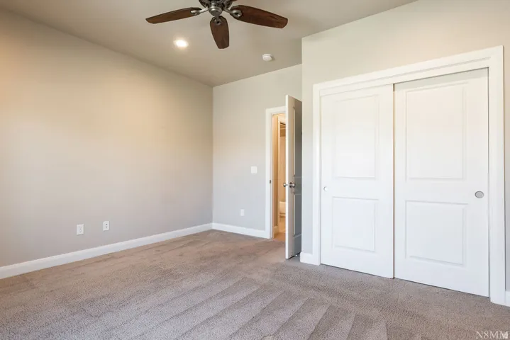 Carpeted flooring, recessed lighting, ceiling fan with wood-finish blades, white sliding closet doors, and a paneled interior door