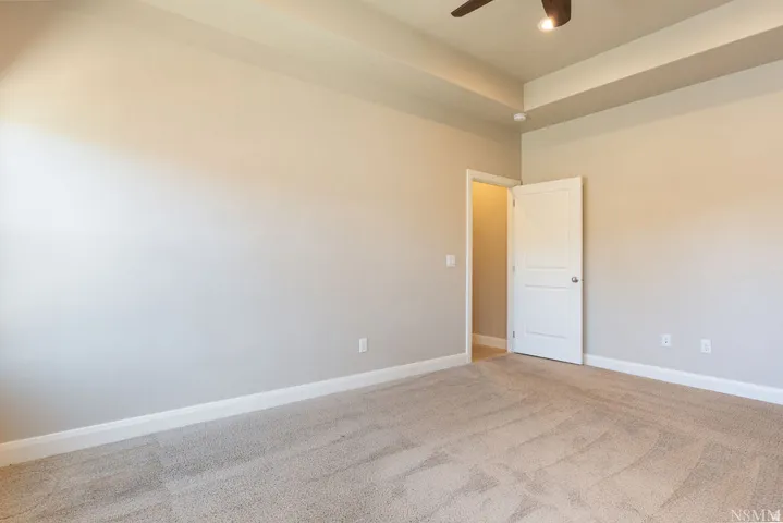 Tray ceiling with a ceiling fan, neutral wall paint, and light-toned carpeting