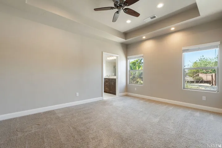 Recessed lighting, ceiling fan, two windows, and an en-suite bathroom featuring a wood-finish vanity