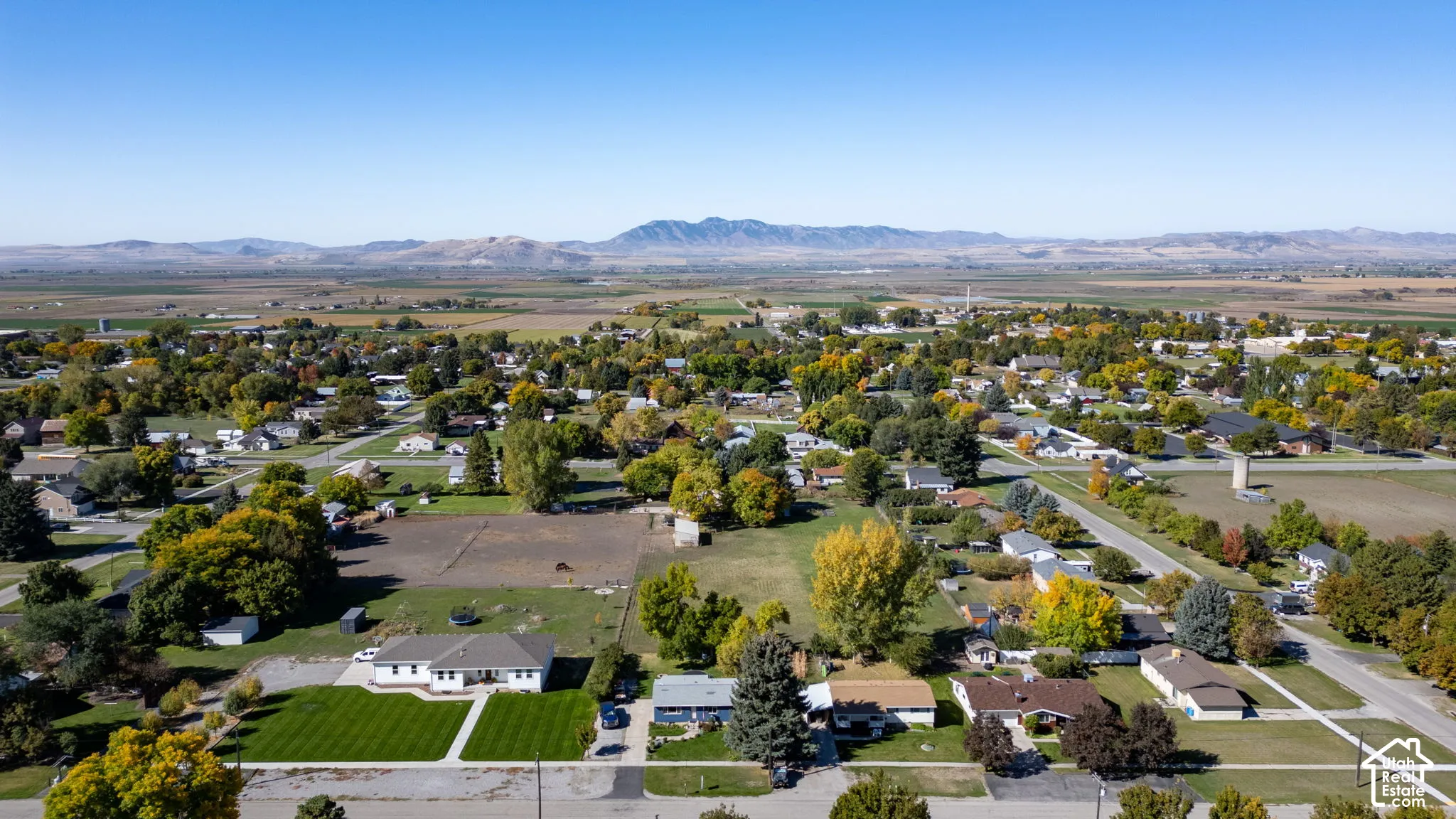 Expansive suburban landscape featuring scattered residential properties, mature trees with seasonal foliage, and distant mountains