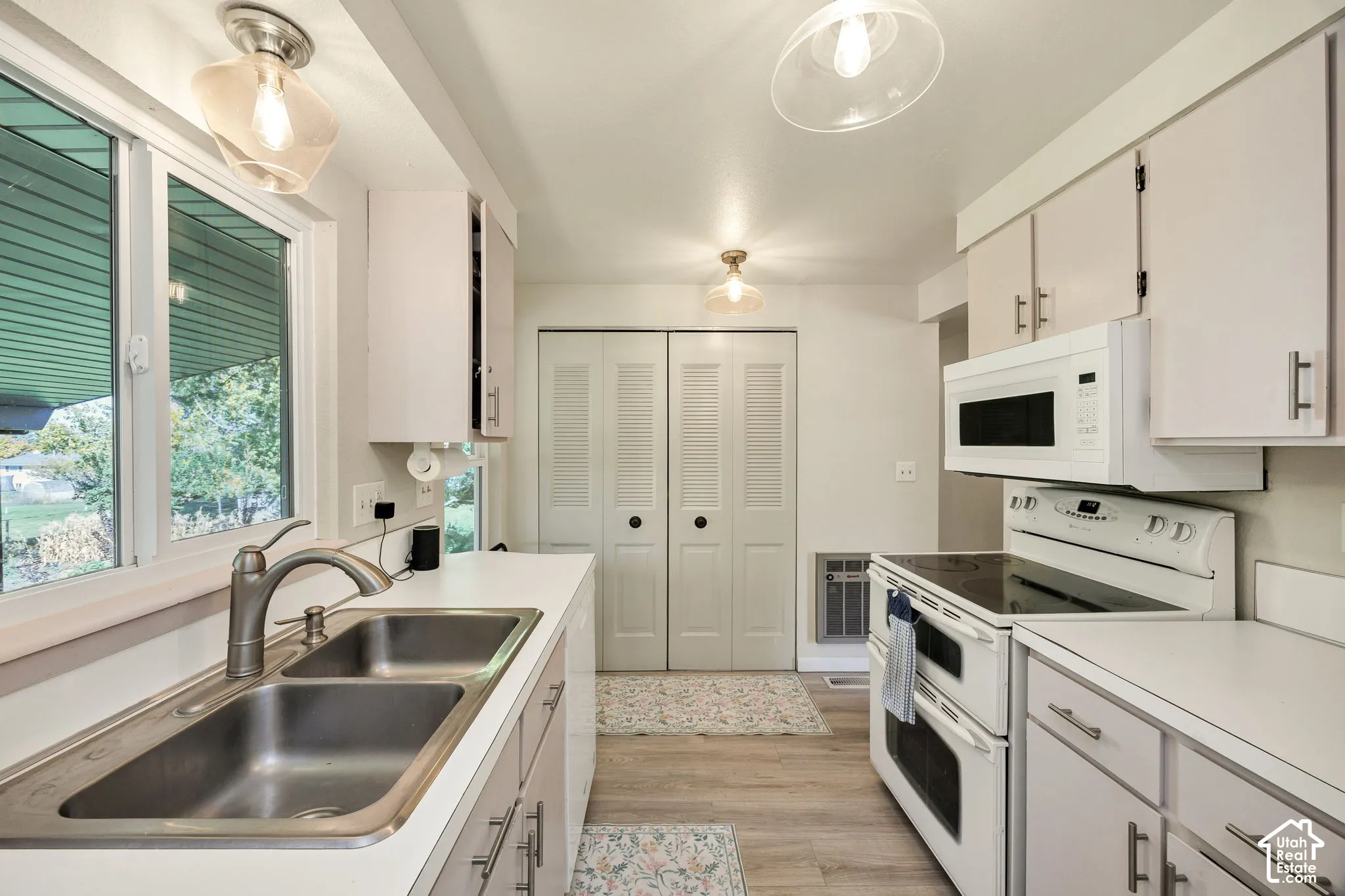Kitchen featuring dual stainless steel sinks, white cabinetry with silver-tone hardware, wood-finish flooring, and white appliances including an electric range and microwave