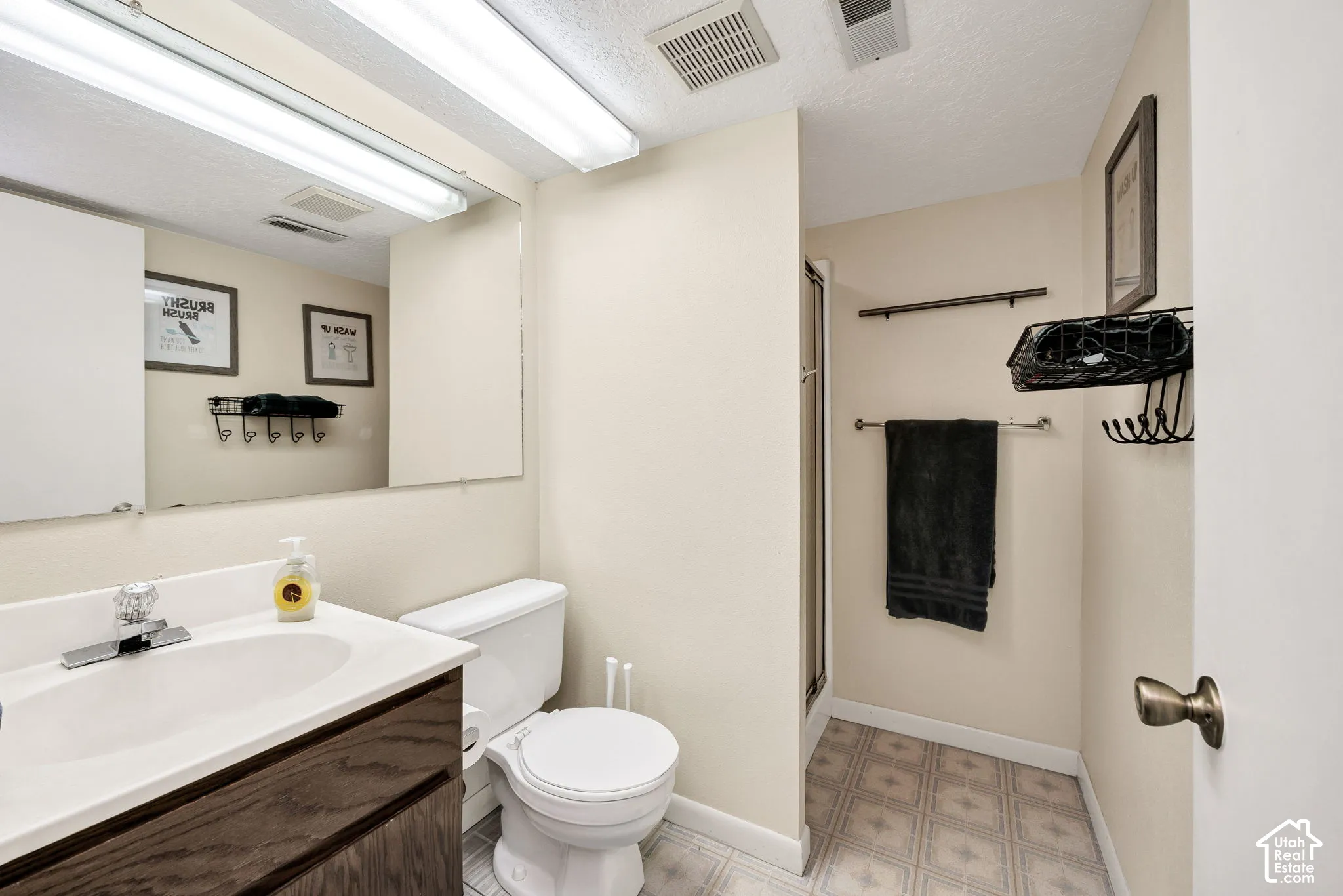 Bathroom with wood-finish vanity, white countertop with integrated sink, rectangular mirror, and a shower enclosure