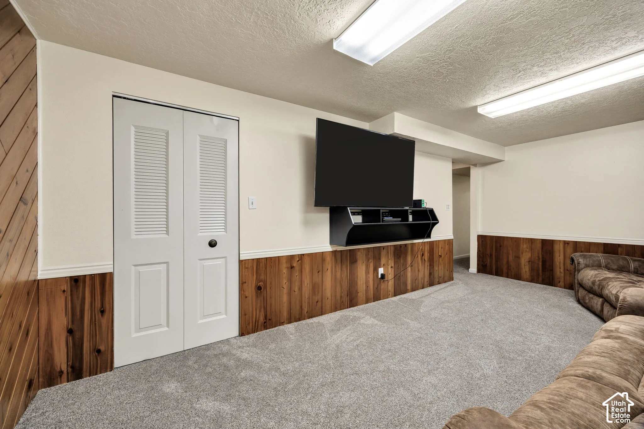 Carpeted flooring, wood paneling, white bi-fold closet doors, wall-mounted media console, and recessed lighting