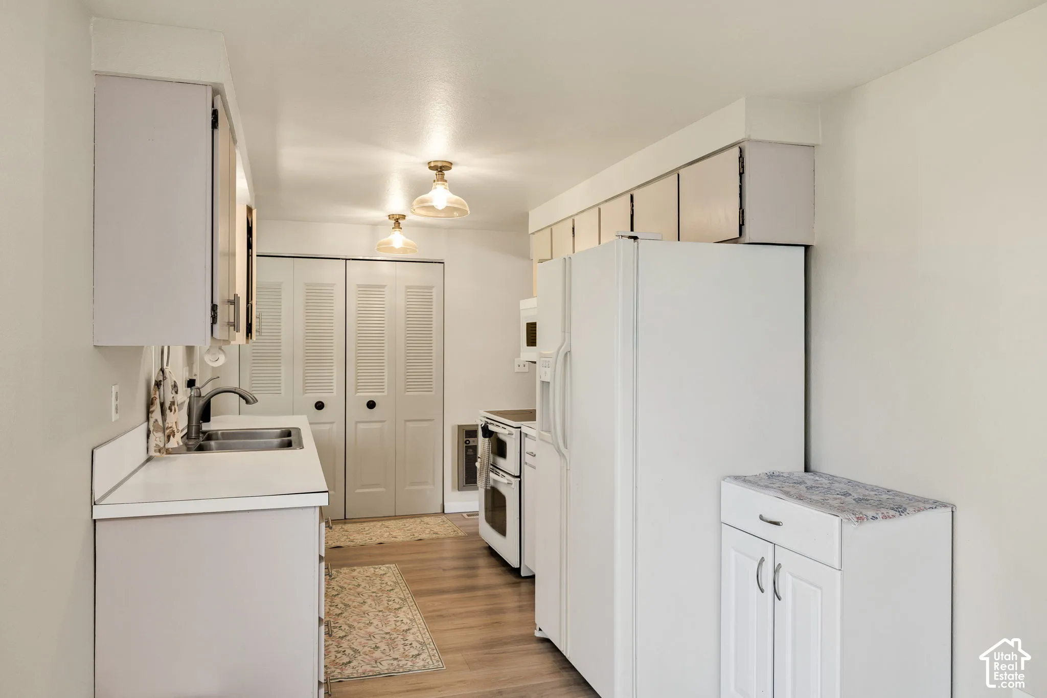 Kitchen featuring wood-finish flooring, white cabinetry, a double basin sink, and bi-fold louvered doors