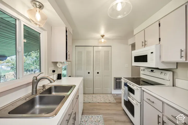 Kitchen featuring dual stainless steel sinks, white cabinetry with silver-tone hardware, wood-finish flooring, and white appliances including an electric range and microwave