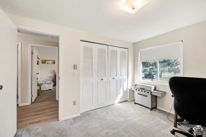 Carpeted room featuring a window with roller shade, louvered bi-fold closet doors, and overhead lighting