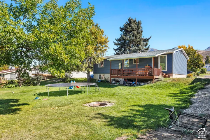 Expansive grass yard with a built-in fire pit, mature trees, and a raised wood-finish deck