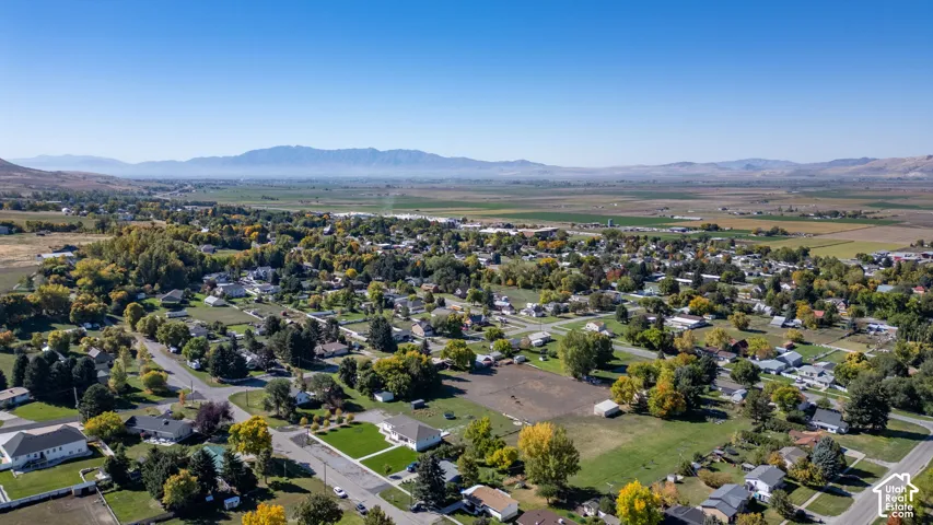 Expansive community with varied residential architecture and mature trees, set against a distant mountain range and agricultural fields