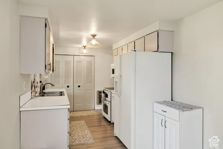 Kitchen featuring wood-finish flooring, white cabinetry, a double basin sink, and bi-fold louvered doors